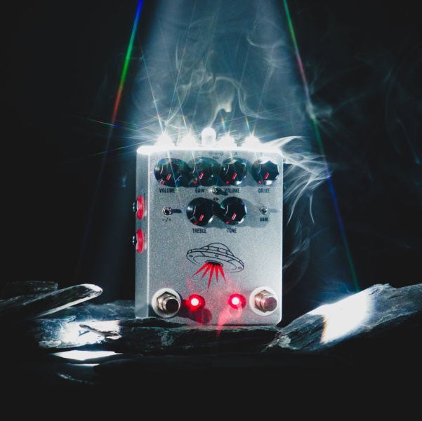 Pedal JHS Wanderer plateado con dibujo de platillo volante sobre piedras oscuras y humo