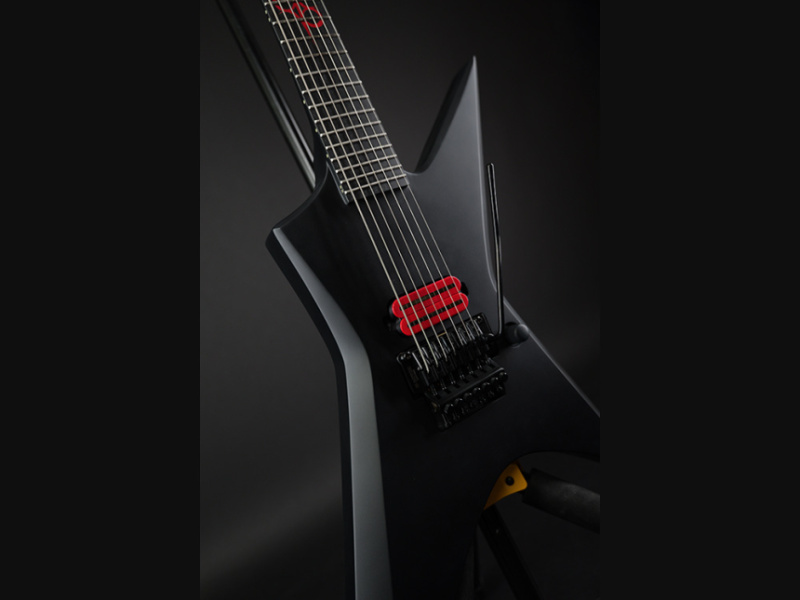 Primer plano del cuerpo con pastilla humbucker roja, vibrato negro y siete cuerdas sobre fondo oscuro