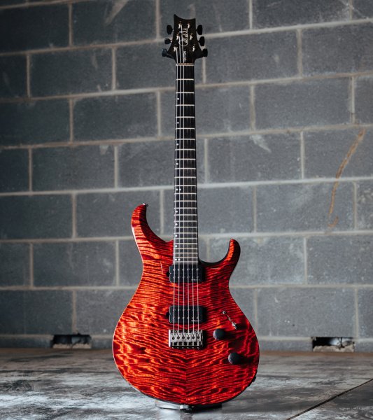 Guitarra PRS Tekton de color Bloodstone Red apoyada en el suelo con pared de bloques de hormigón gris detrás