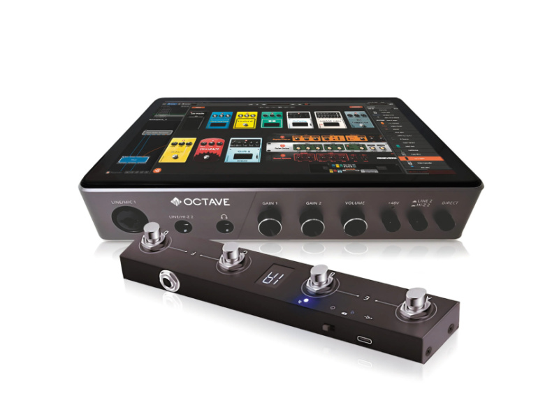 Caja gris oscura del Octave HS-1 con pantalla táctil encendida mostrando pedales y racks de efectos, frontal con logotipo, entradas, salidas y mandos, junto a una pedalera negra alargada con cuatro pulsadores metálicos.