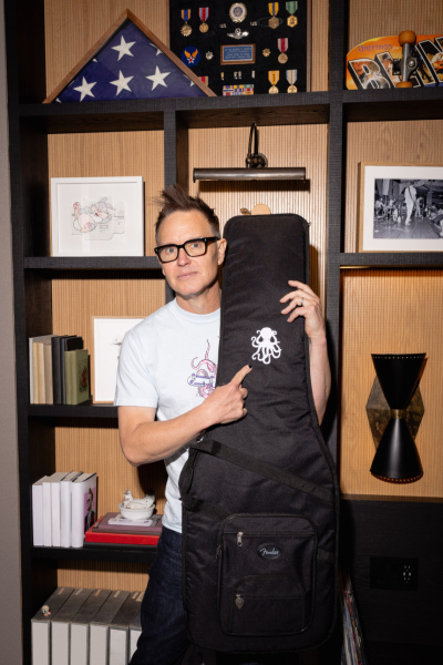 Mark Hoppus de pie sujetando una funda negra con un pulpo blanco bordado