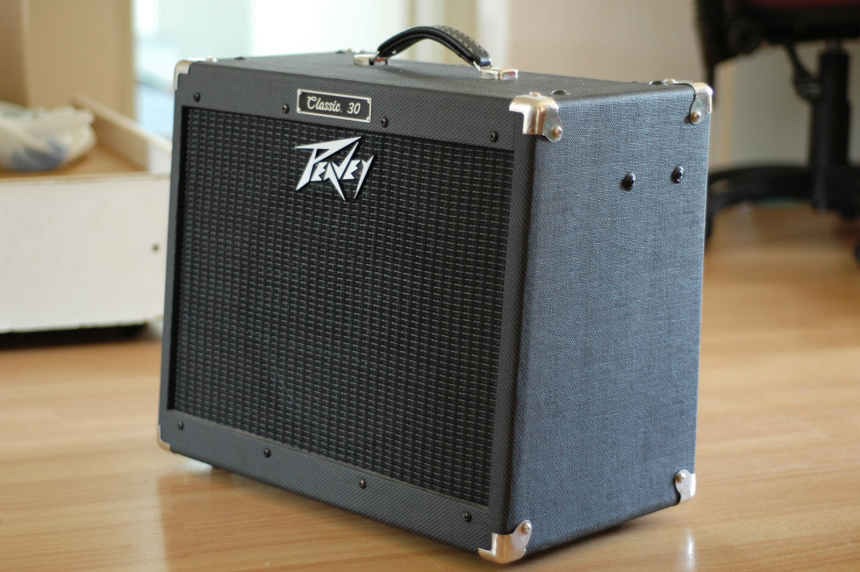Vista de tres cuartos del combo de guitarra Peavey Classic 30 con tólex negro tipo tweed y rejilla negra sobre suelo de madera.