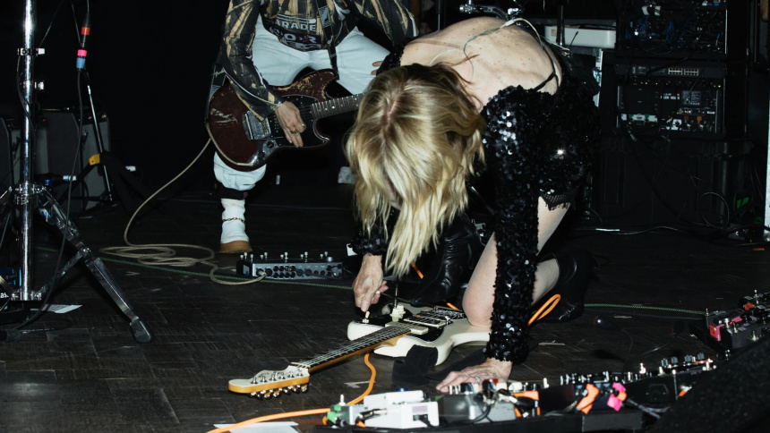 Kim Gordon tocando arrodillada sobre su Jazzmaster apoyada en el suelo