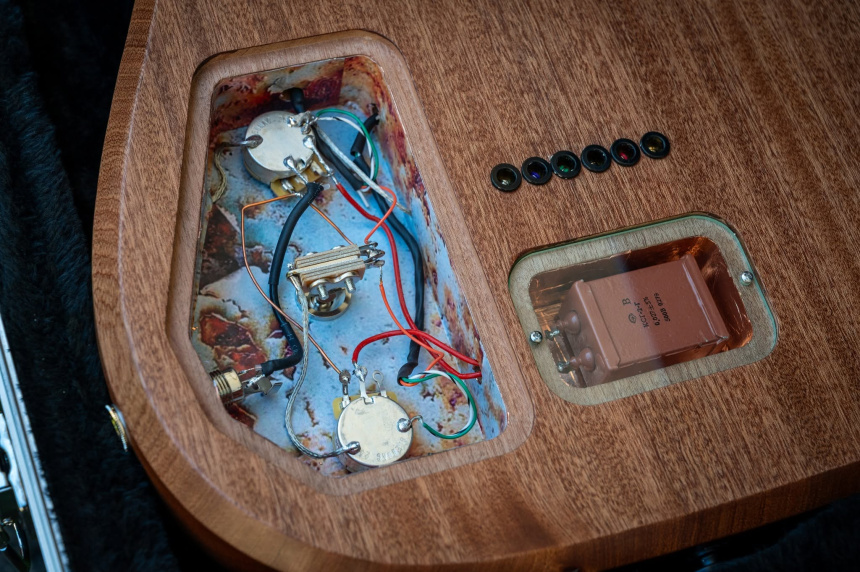 Trasera de la guitarra con cavidad electrónica abierta, potenciómetros y compartimento del condensador KSG-2G bajo tapa transparente.