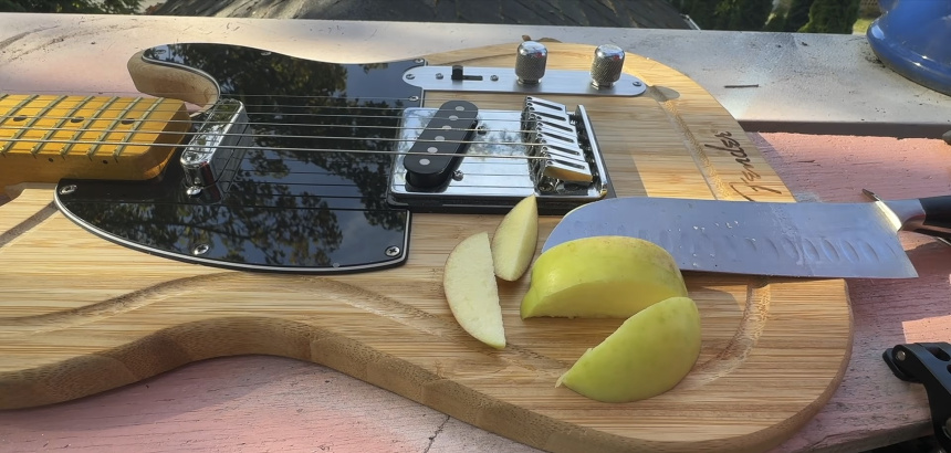La guitarra terminada con trozos de manzana y cuchillo de cocina sobre la parte libre de la tabla, al aire libre.